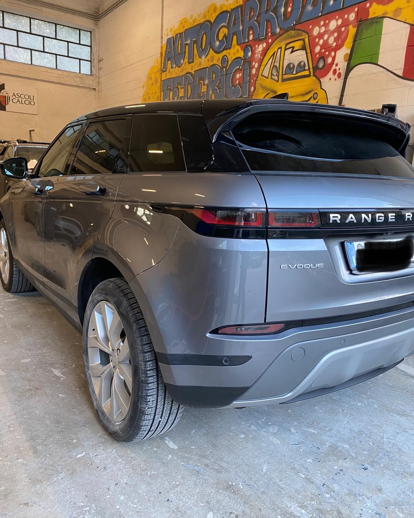 Un SUV Range Rover grigio parcheggiato in un garage con un murale sullo sfondo.