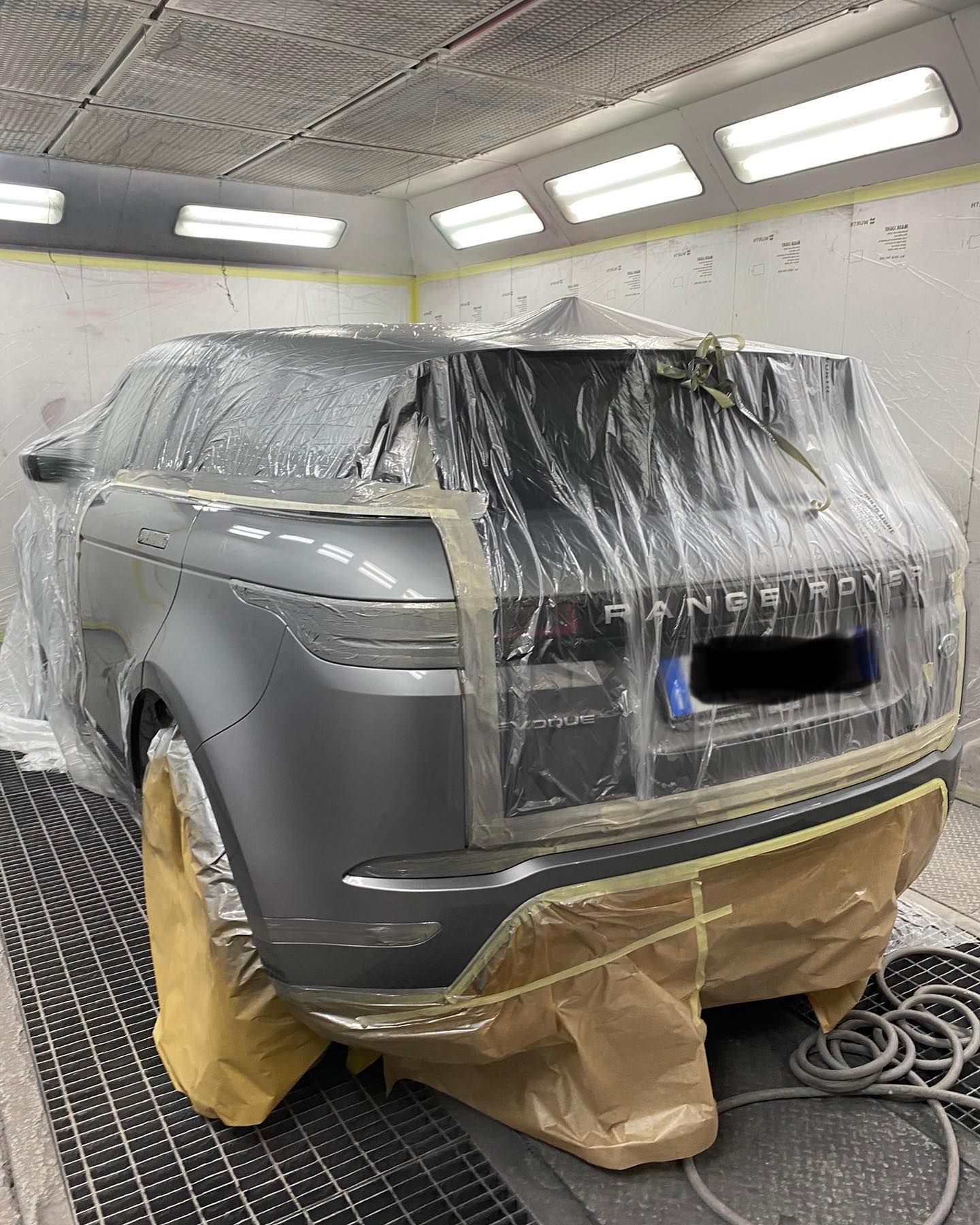 Un SUV Range Rover grigio in una cabina di verniciatura, coperto di plastica e isolato con nastro adesivo per la verniciatura.