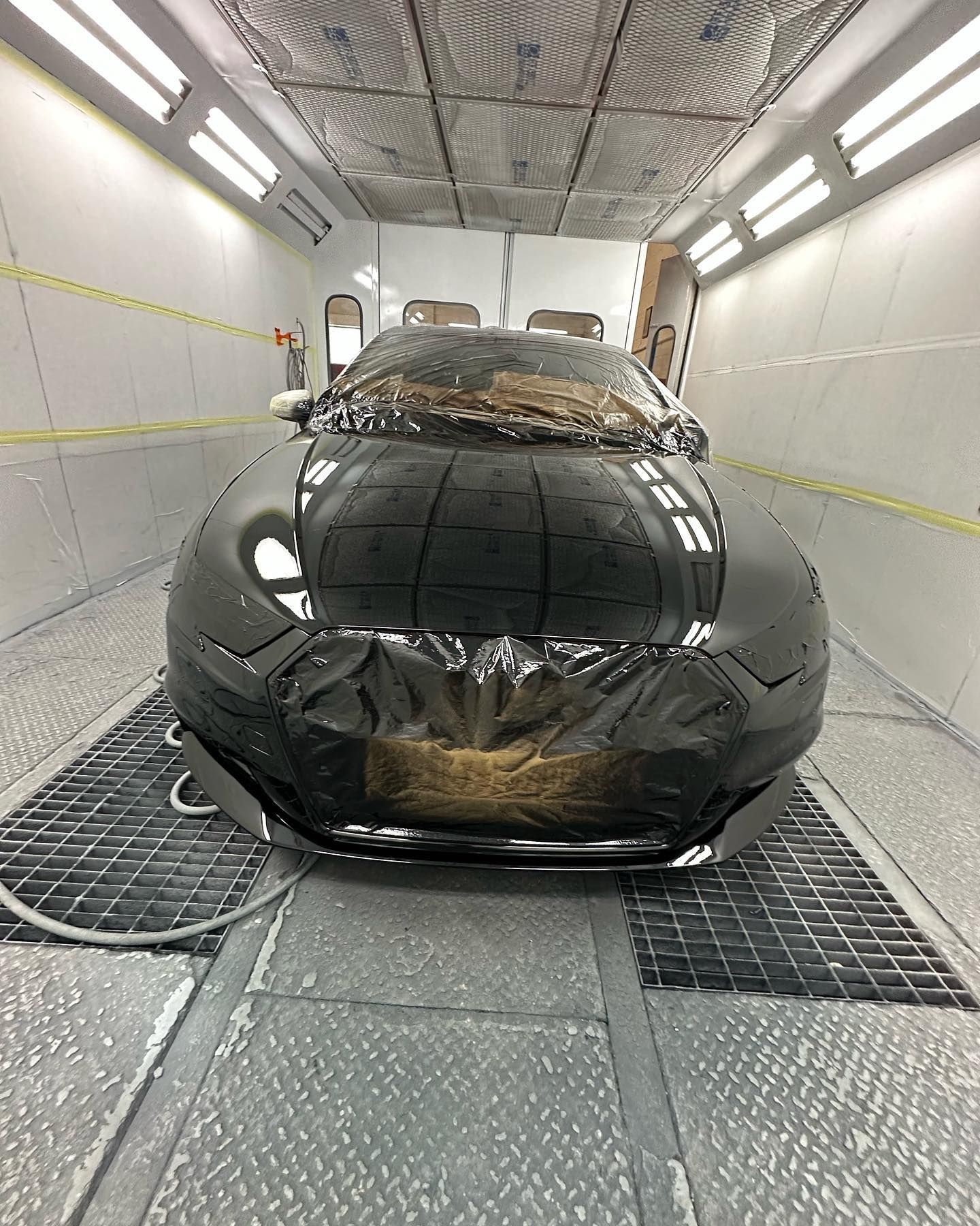 Auto nera in una cabina di verniciatura, ricoperta da pellicola protettiva.