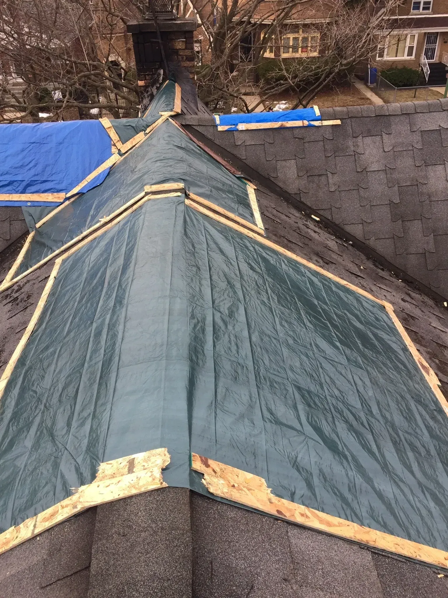 Partially tarped roof with wooden supports; green and blue tarps.
