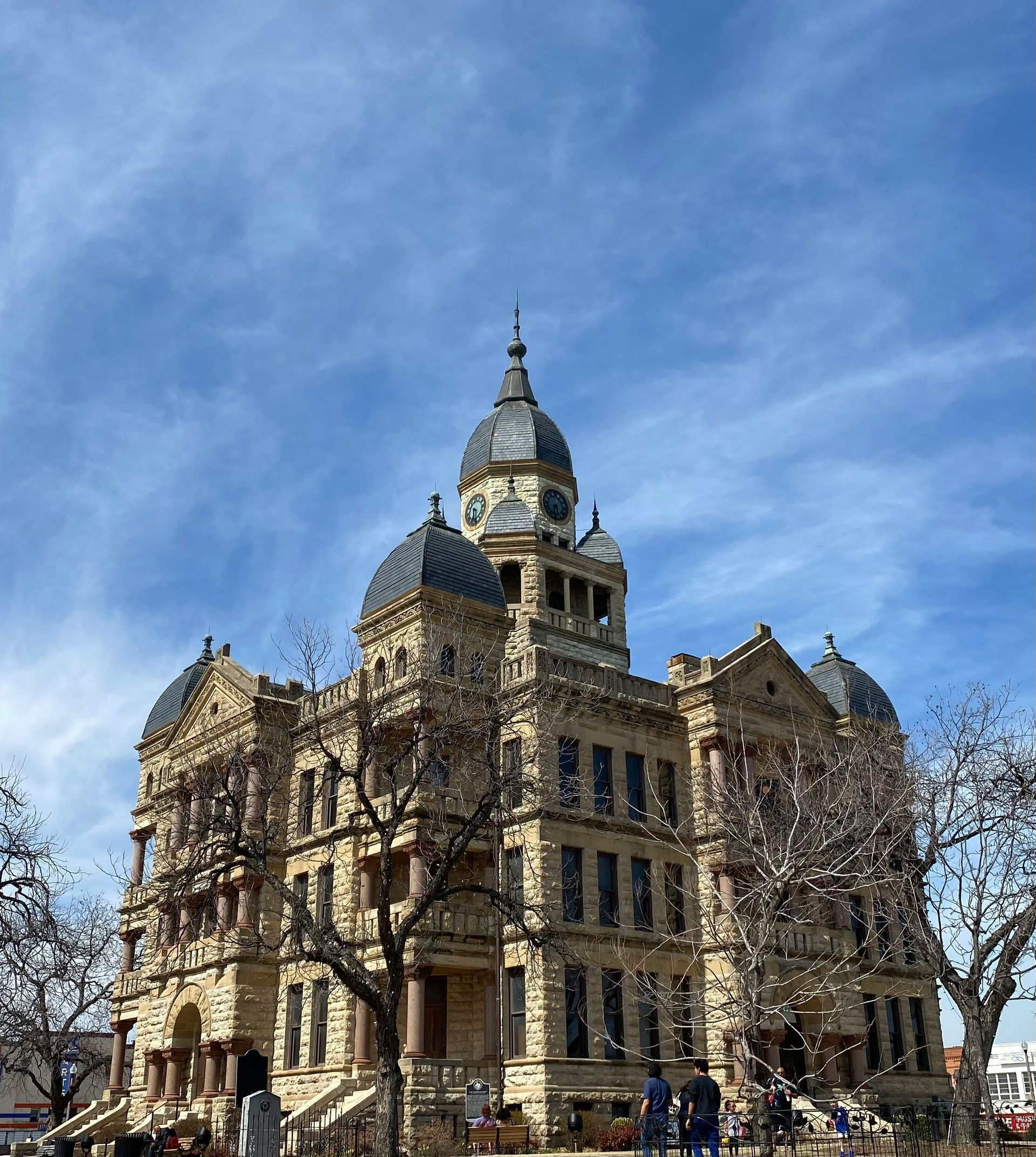 Historic stone courthouse with ornate dome under a blue sky, people gathered at the entrance