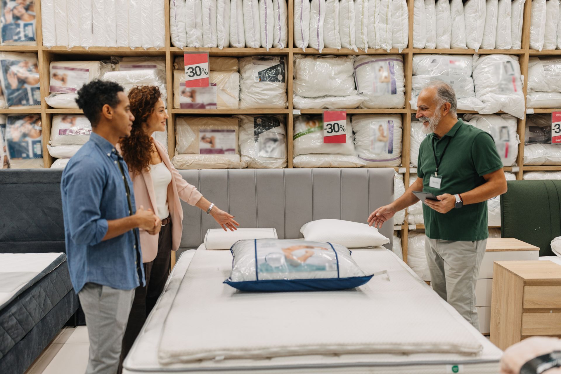 Two individuals explore mattress options, engaging with a sales representative.
