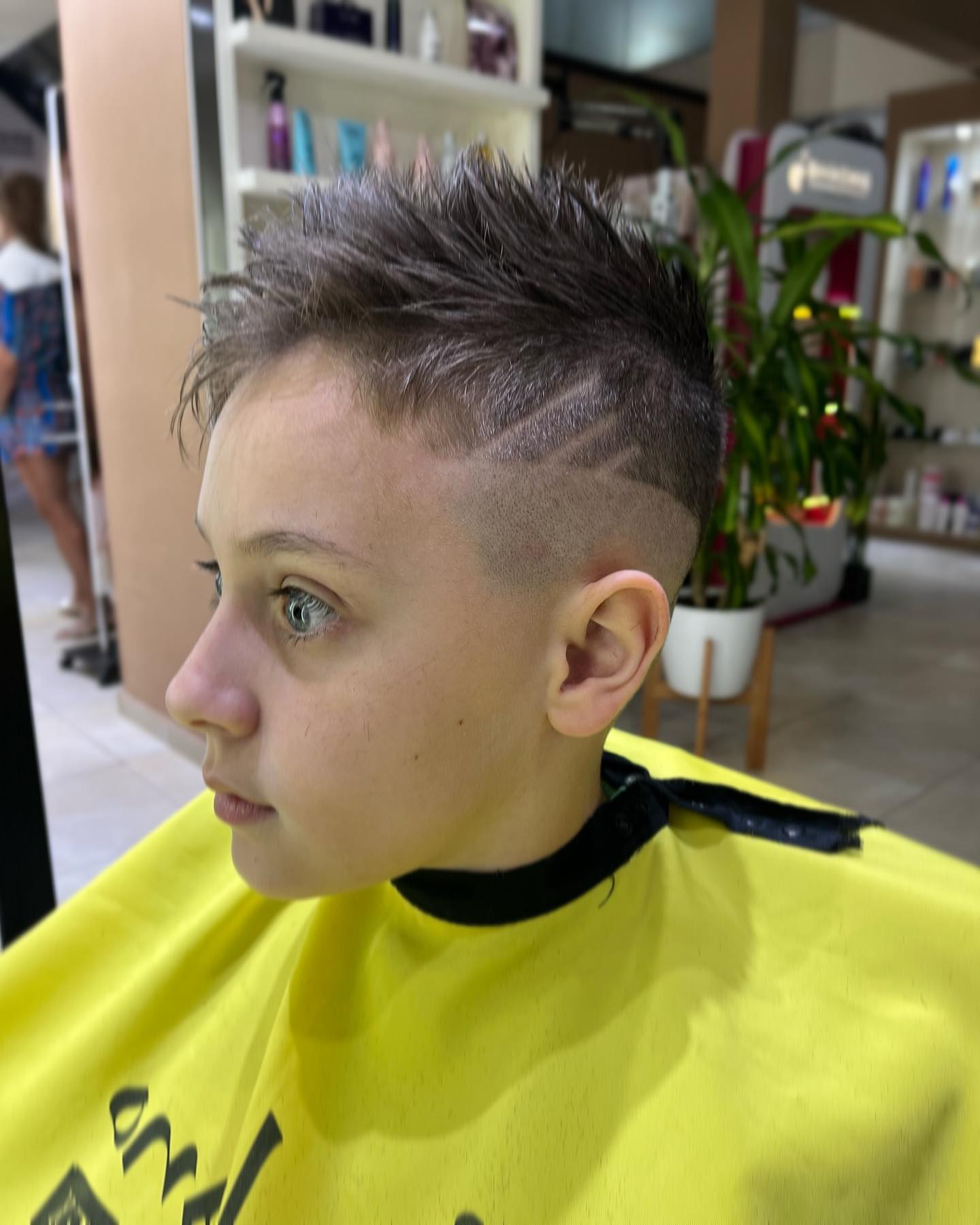 Perfil de una persona con el pelo corto y texturizado, con un diseño rapado en la sien y que lleva una capa amarilla.