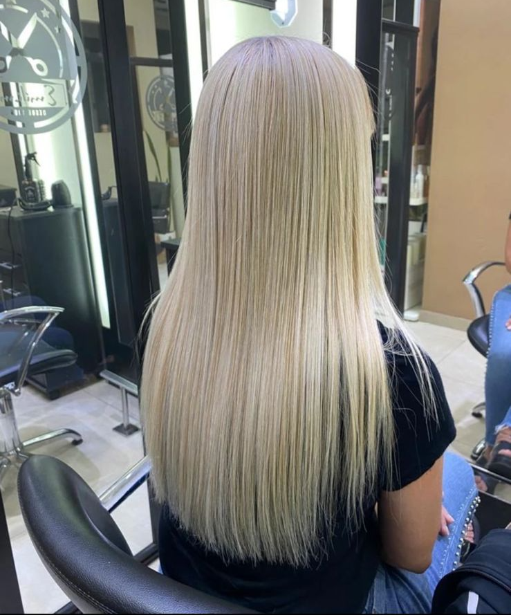 Una persona con cabello largo, liso y rubio platino sentada en una silla de peluquería.