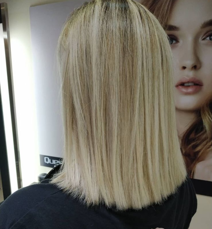 Vista trasera de una persona con cabello rubio liso hasta los hombros en un salón de belleza.