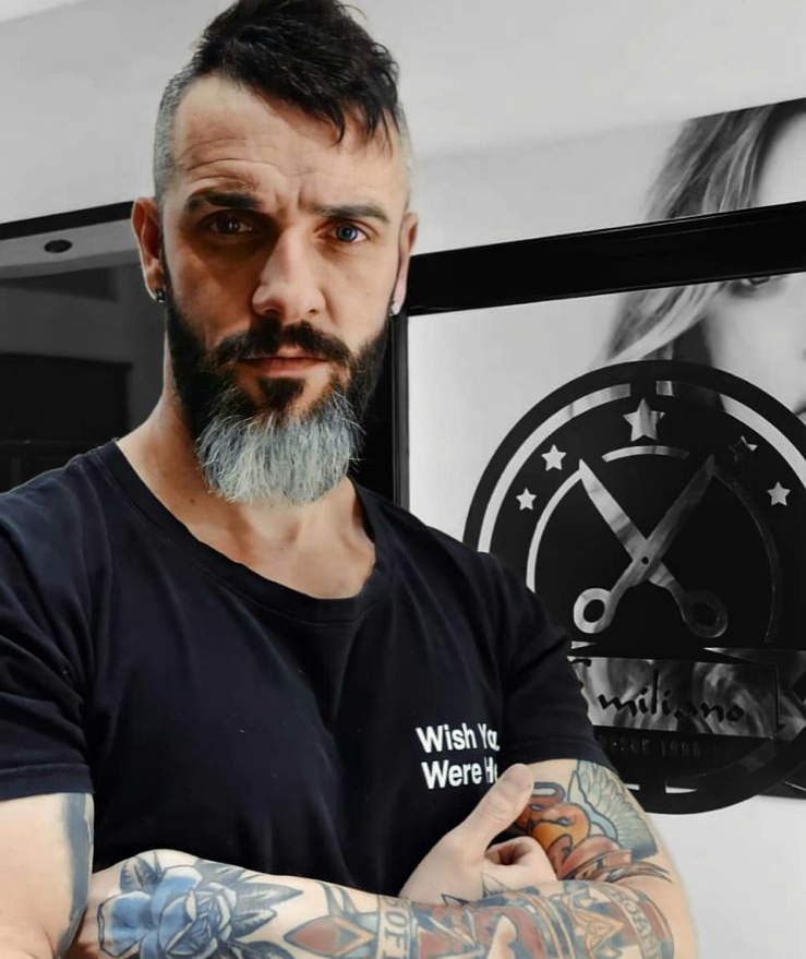 Un barbero tatuado con barba entrecana permanece de pie 