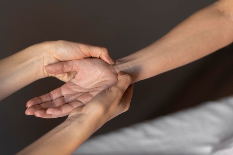 Hands holding and massaging a wrist against a dark background