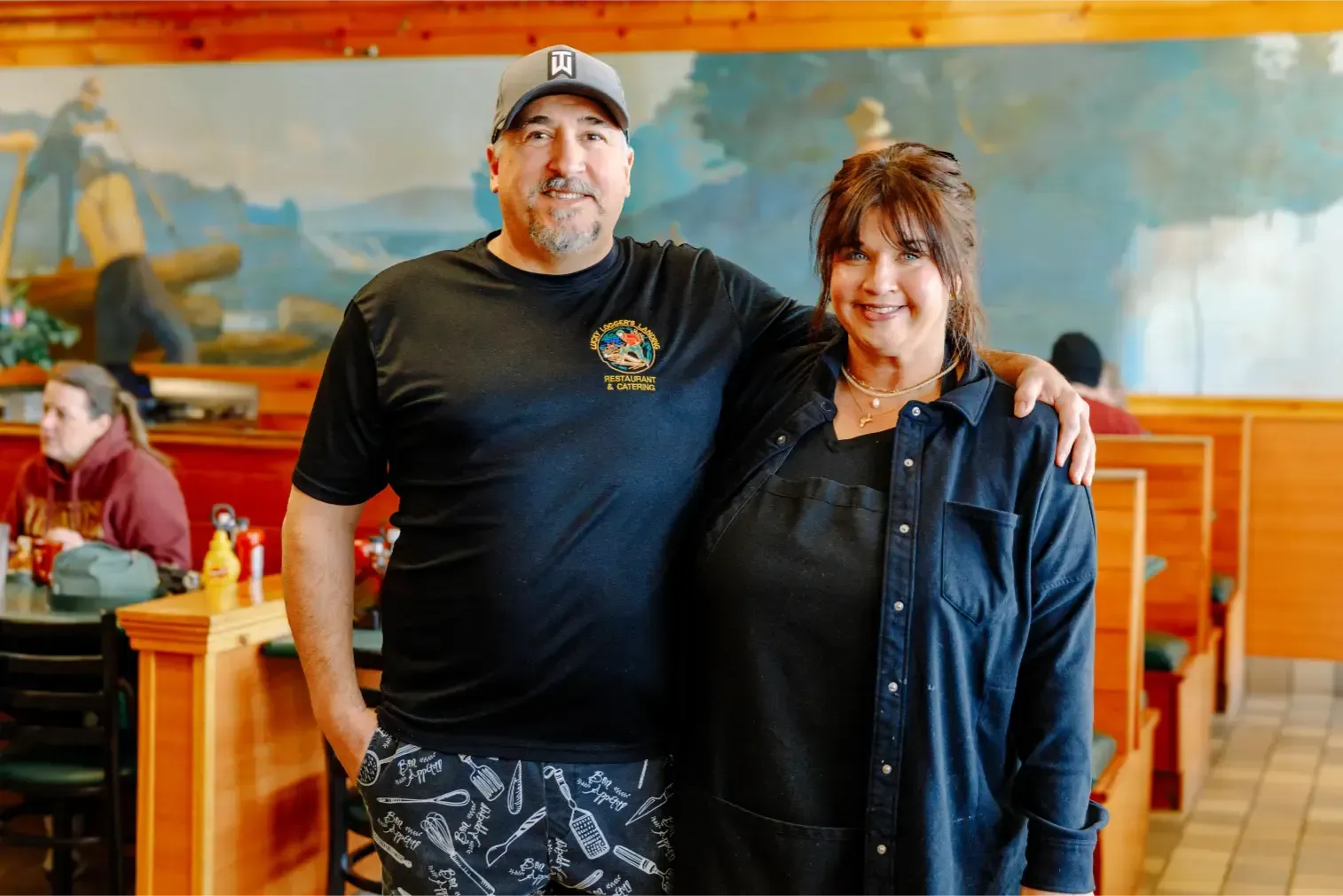 Two people standing together in a restaurant, smiling near orange booths and wooden walls
