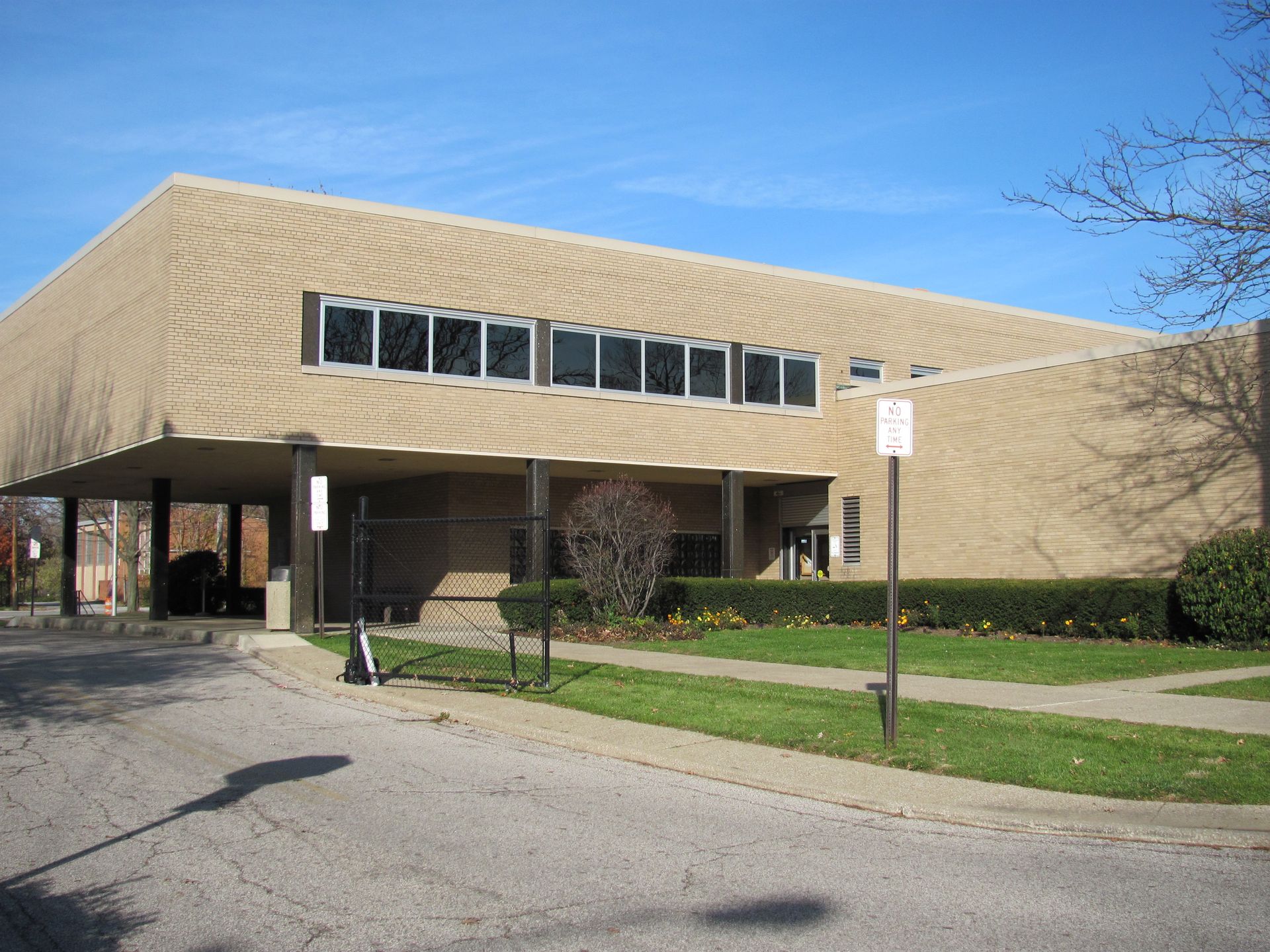 Beige brick building with a flat roof, row of windows, and a small covered entrance.