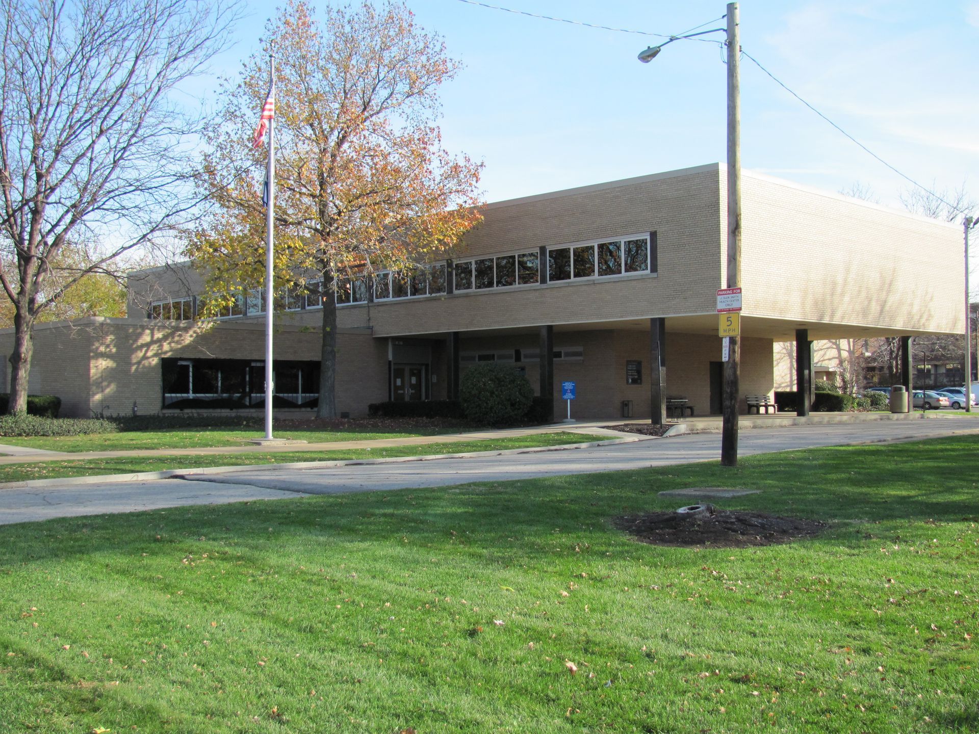 Building with flat roof and long windows, flagpole. Grass lawn in front.