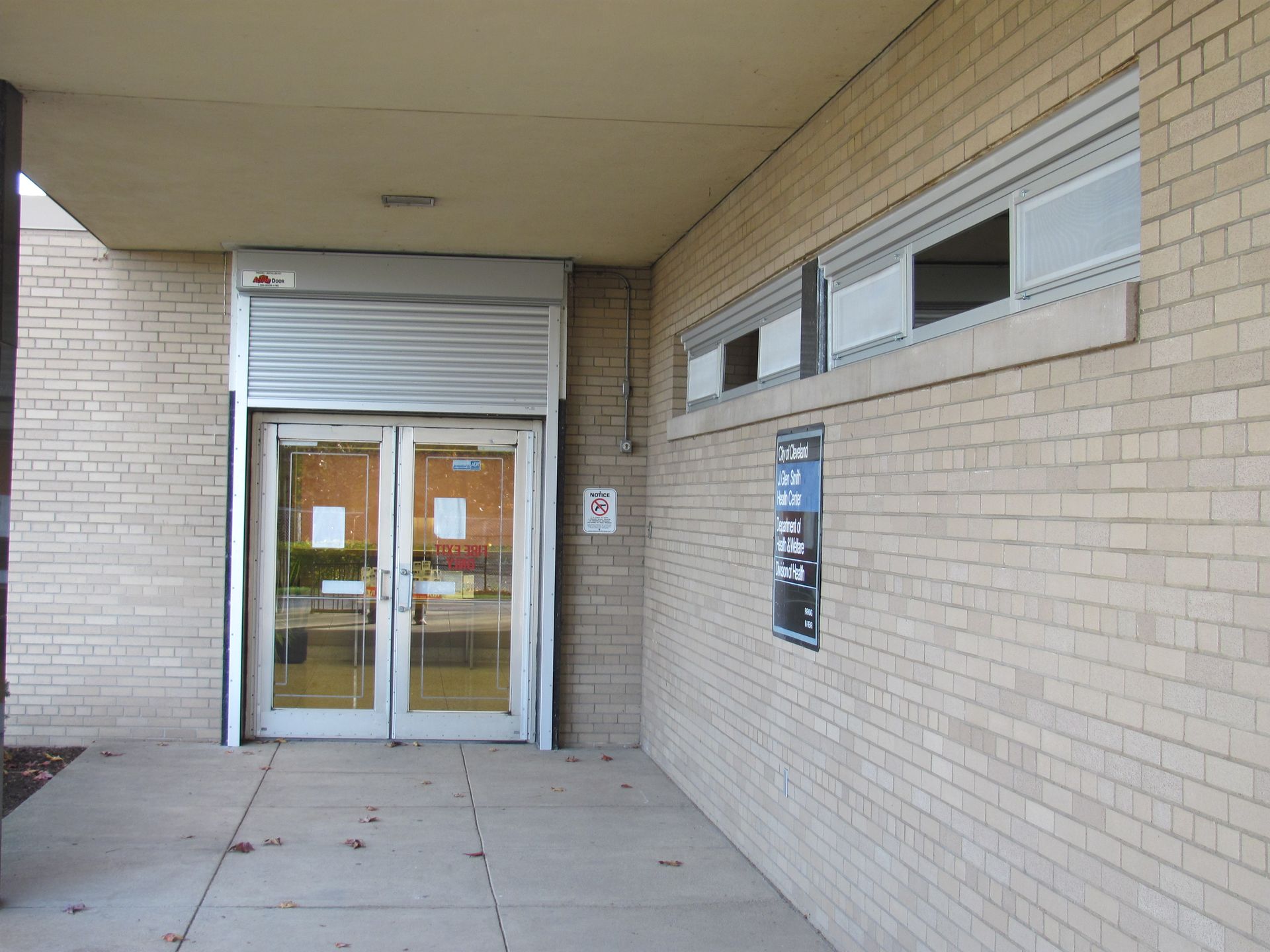 Entrance to a brick building with glass doors, a security shutter, and windows.