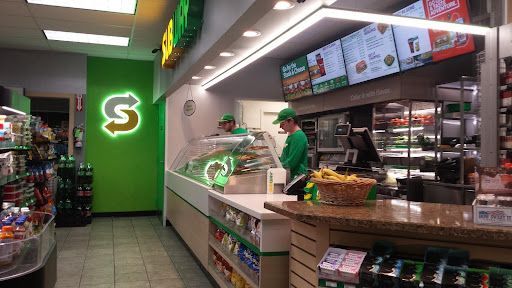 A man is standing at a counter in a subway restaurant.