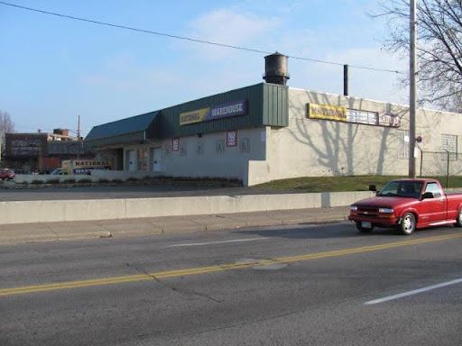 A red truck is driving down the road in front of a building