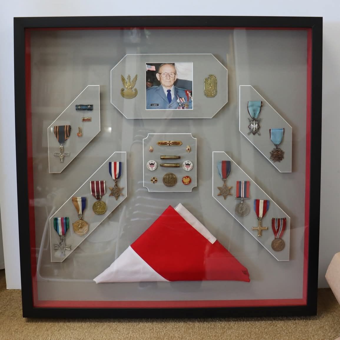 A shadow box display featuring a military portrait, various service medals and pins, and a folded ceremonial flag.