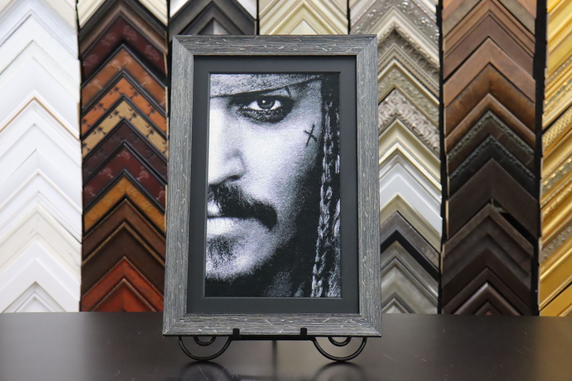 A black-and-white print of Jack Sparrow in a rustic grey frame, set against a background wall of various frame samples.