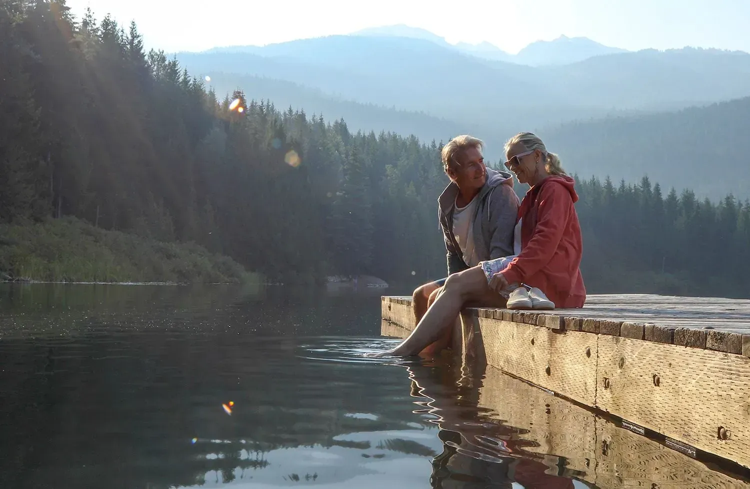 A man and a woman are sitting on a dock overlooking a lake.