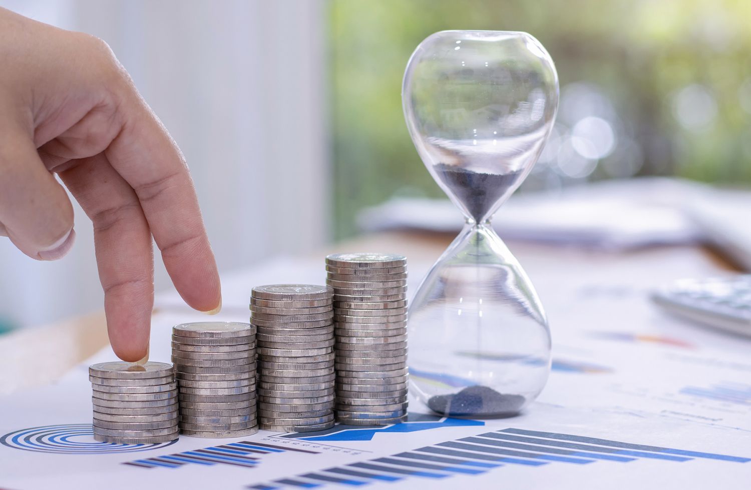 A person is stacking coins next to an hourglass on a table.