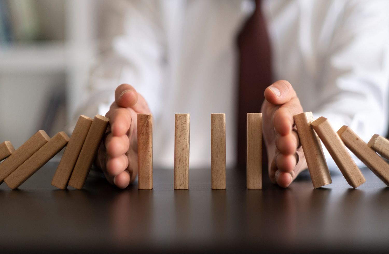 A person is holding wooden blocks in their hands to stop them from falling on a table.