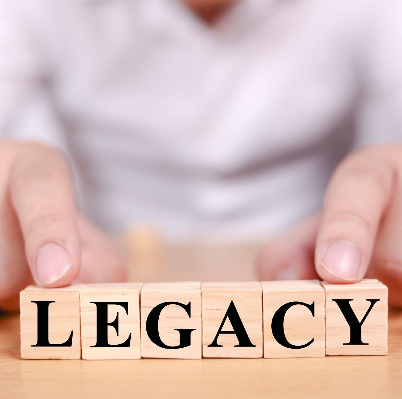 A person is holding wooden blocks that spell out the word legacy