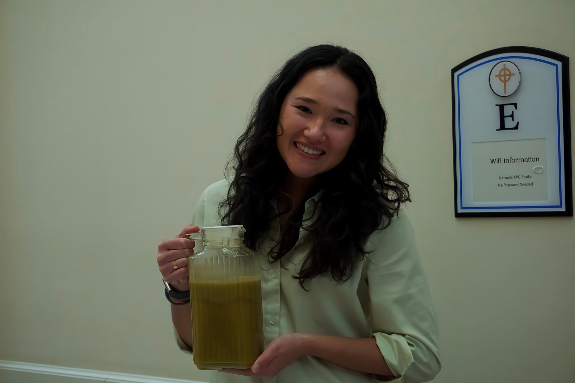 A woman is holding a pitcher of liquid in front of a sign that says e.