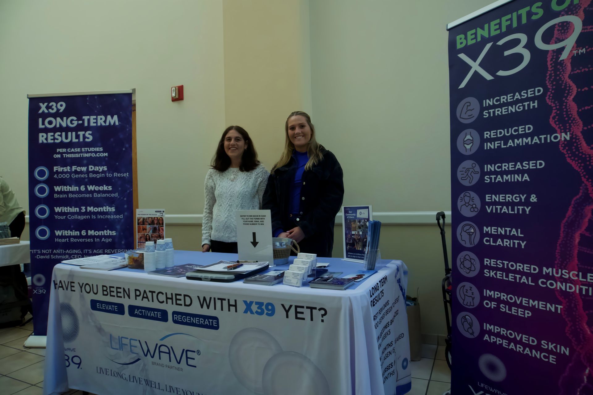 Two women standing behind a table with a sign that says benefits of x39