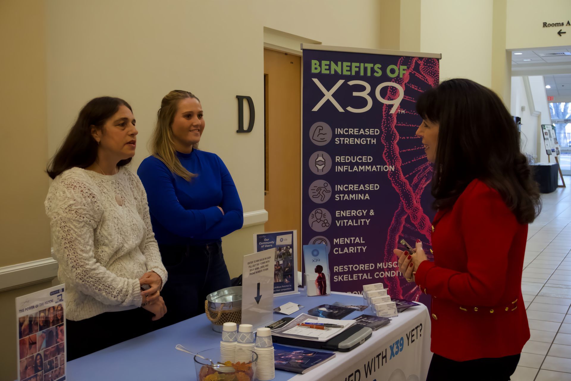 Three women are standing around a table with a sign that says benefits of x39