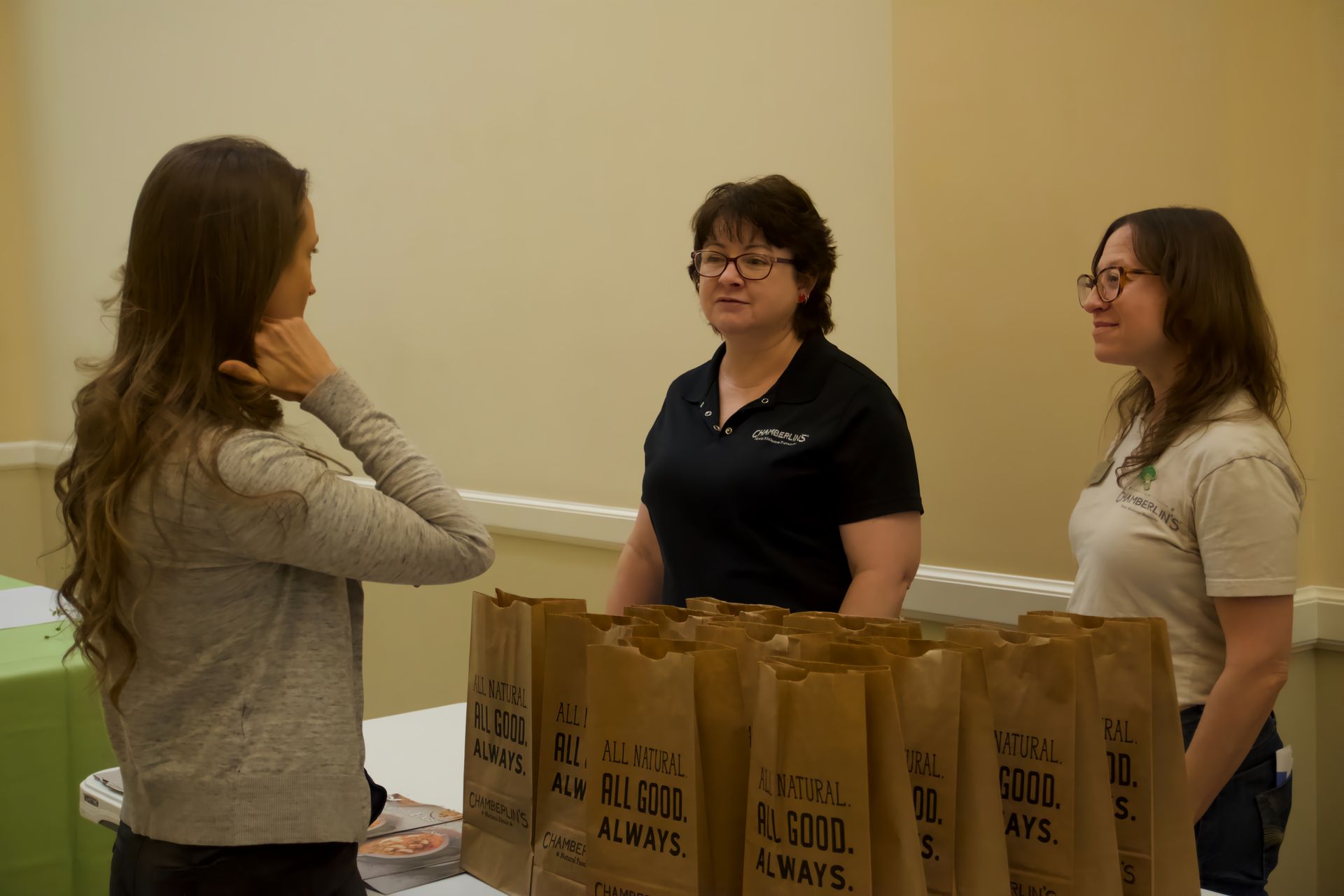Three women are standing around a table talking to each other.