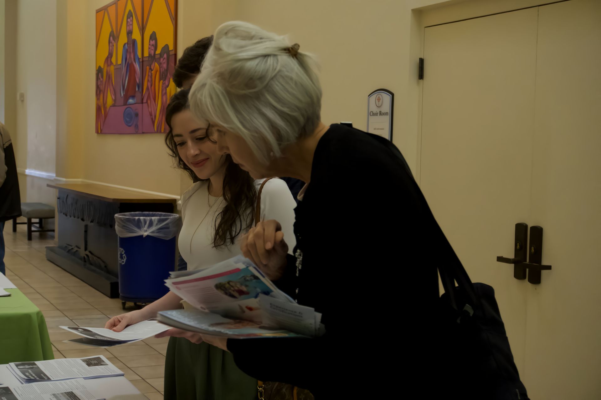 Two women are looking at a magazine in a hallway.