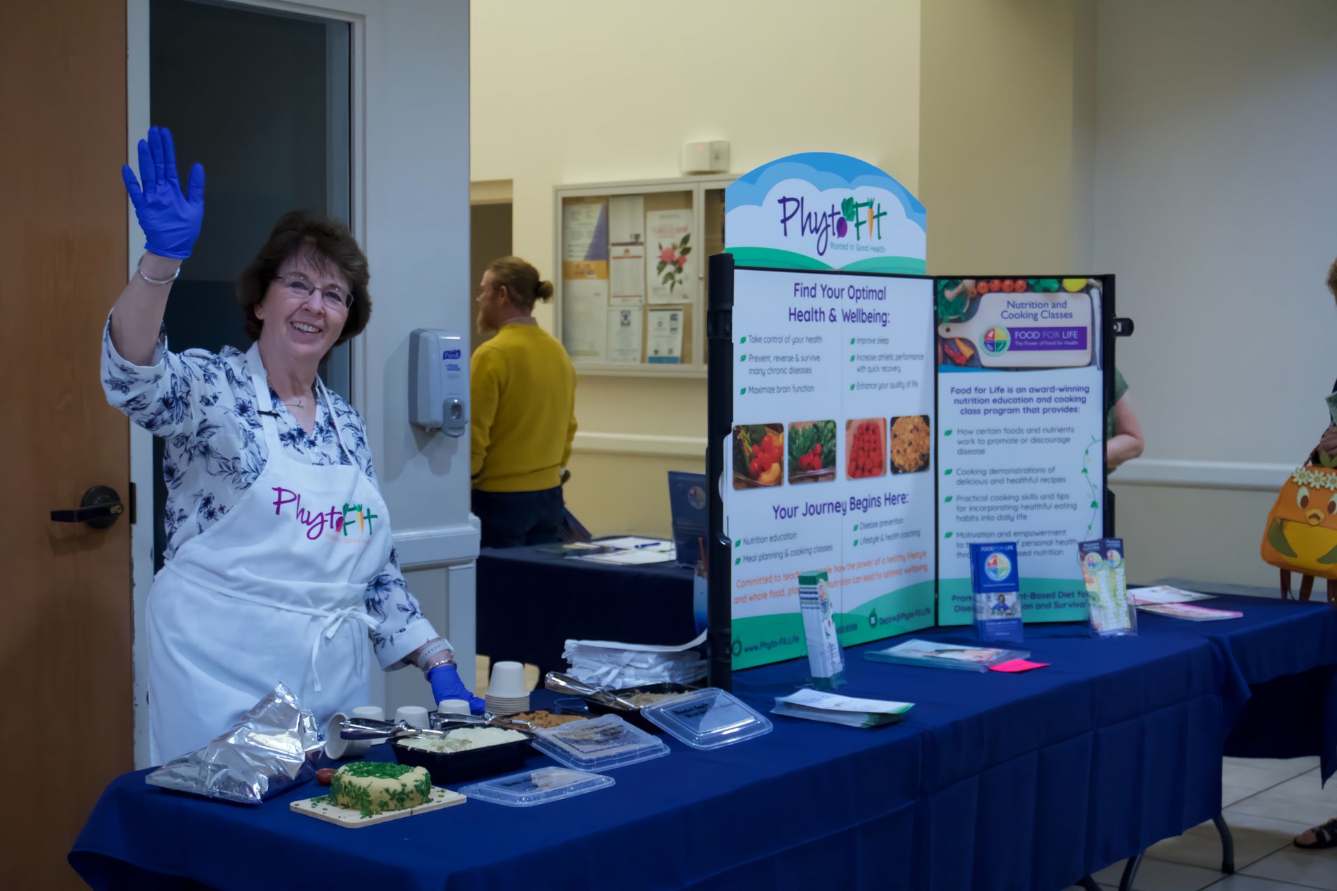 A woman wearing blue gloves is standing in front of a table.