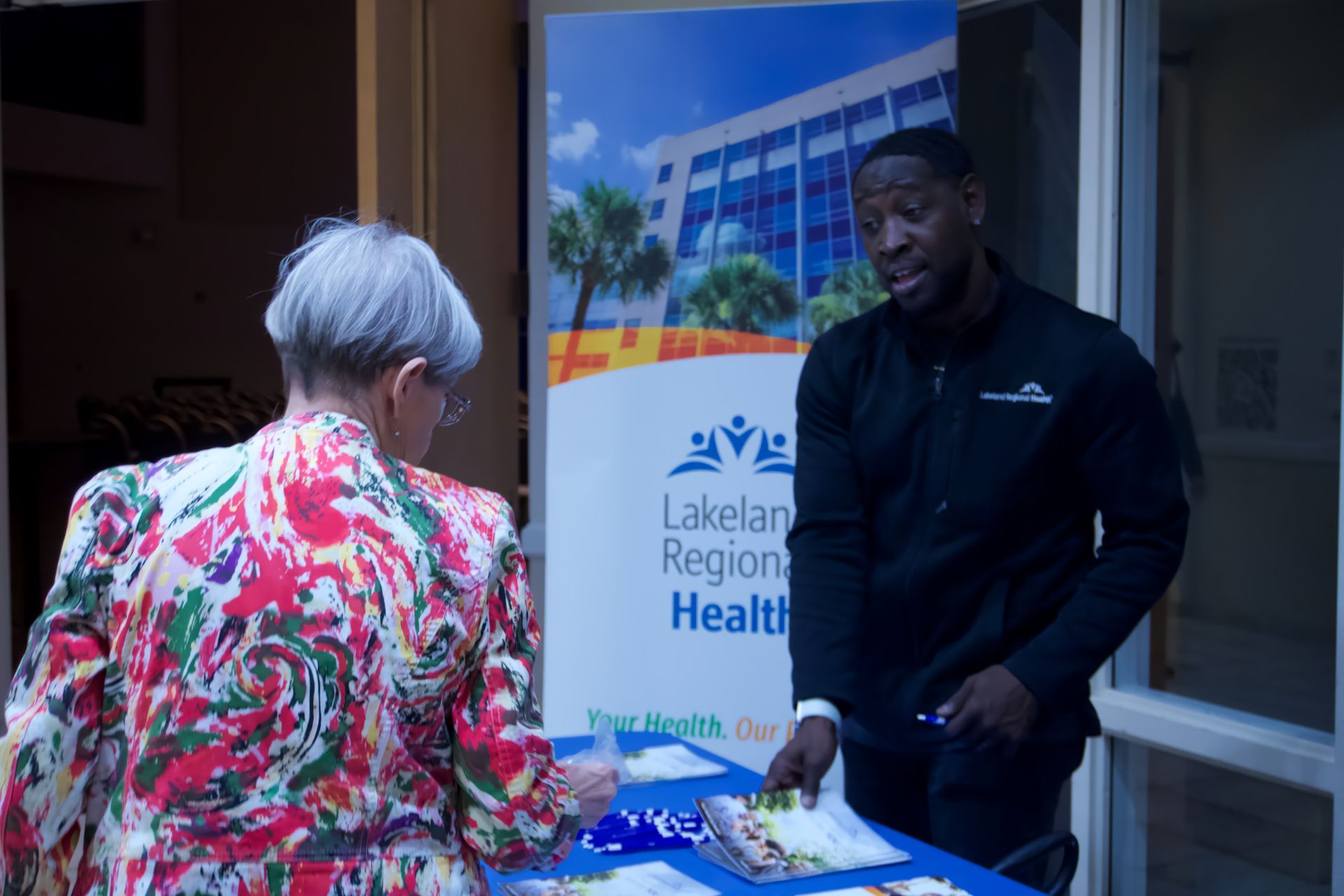 A man is talking to a woman at a table in front of a sign that says lakeland region health