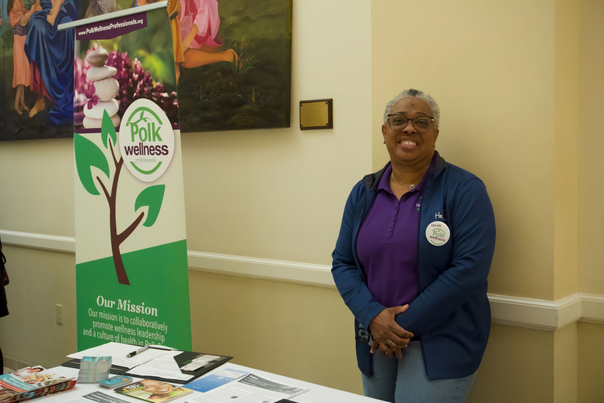 A woman in a purple shirt is standing in front of a table.