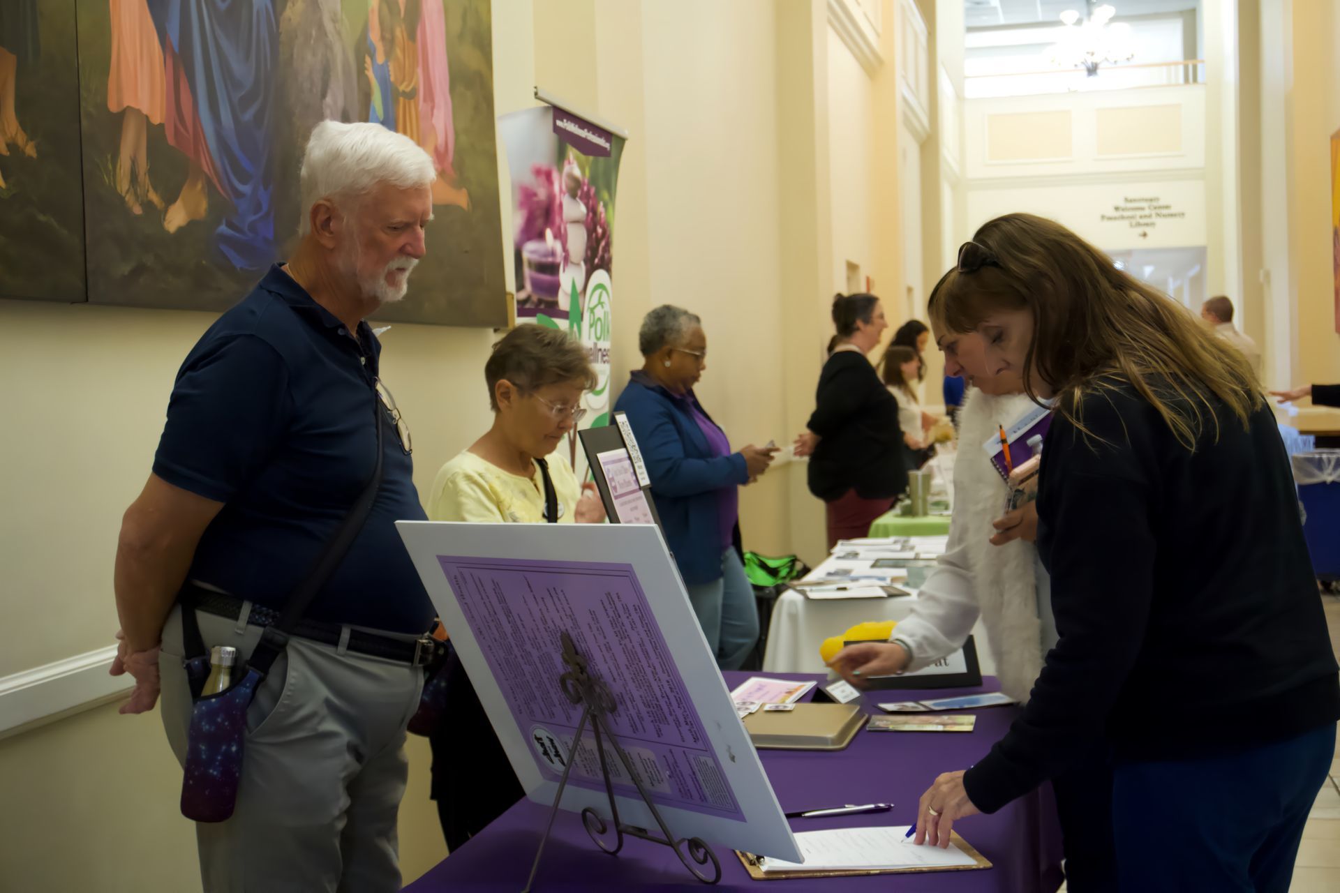 A group of people are standing around a table looking at a painting.