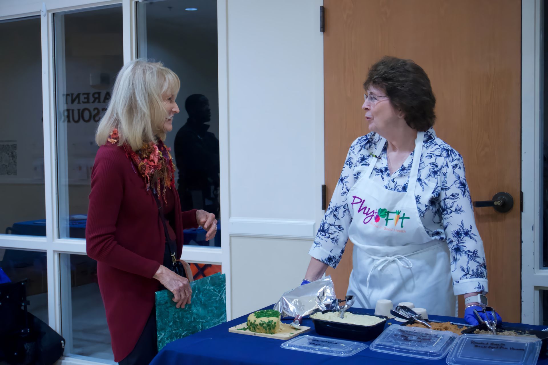 Two women are standing at a table talking to each other.