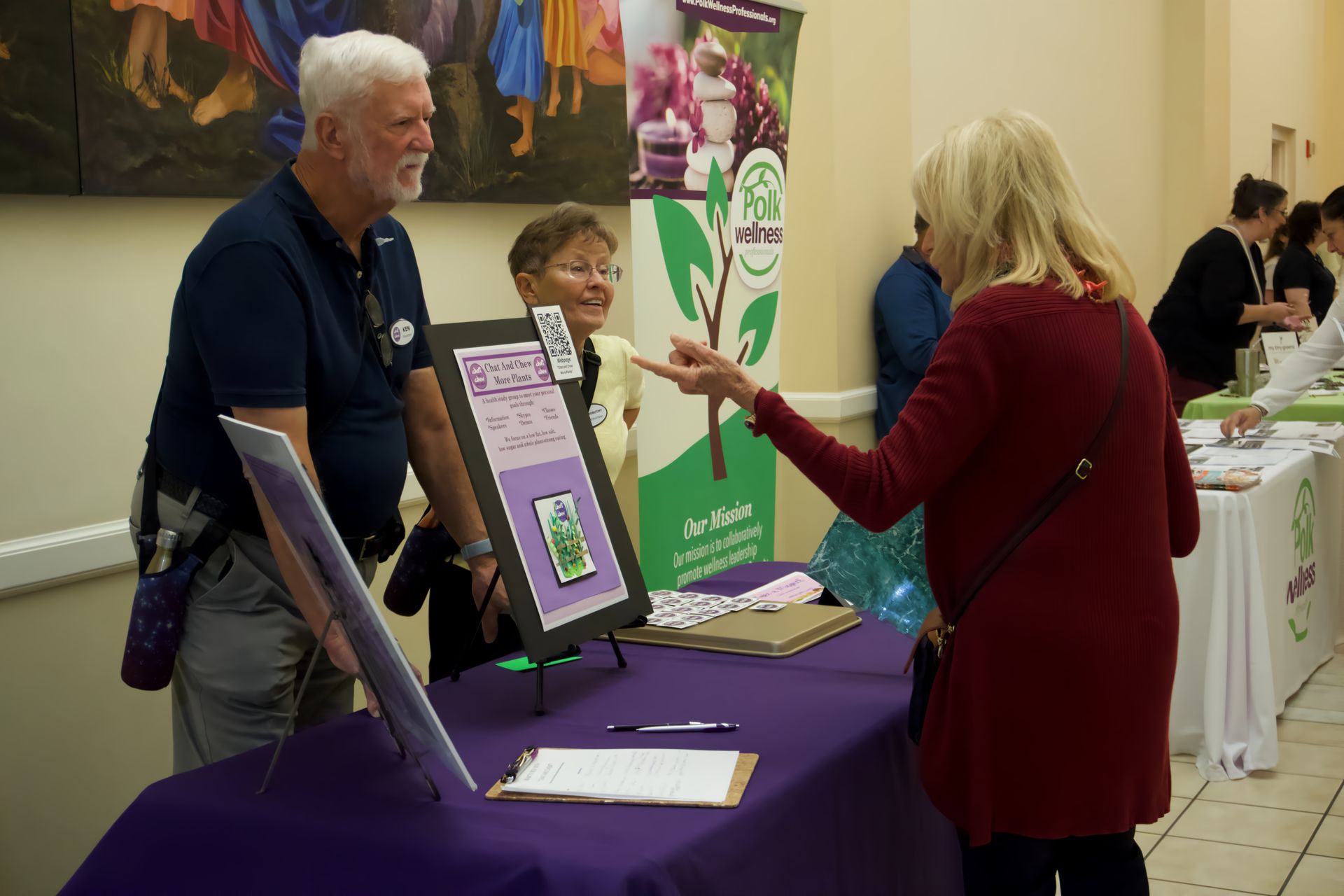 A man and a woman are standing at a table talking to each other.