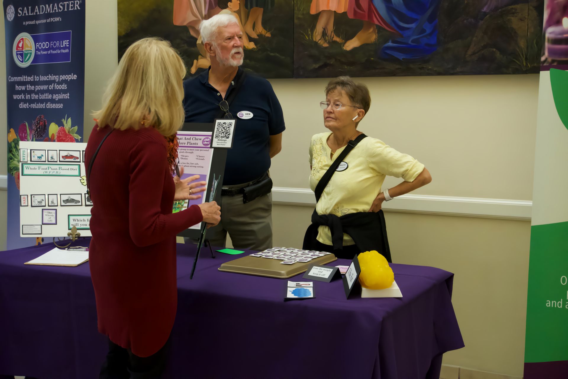 A group of people are standing around a table talking to each other.