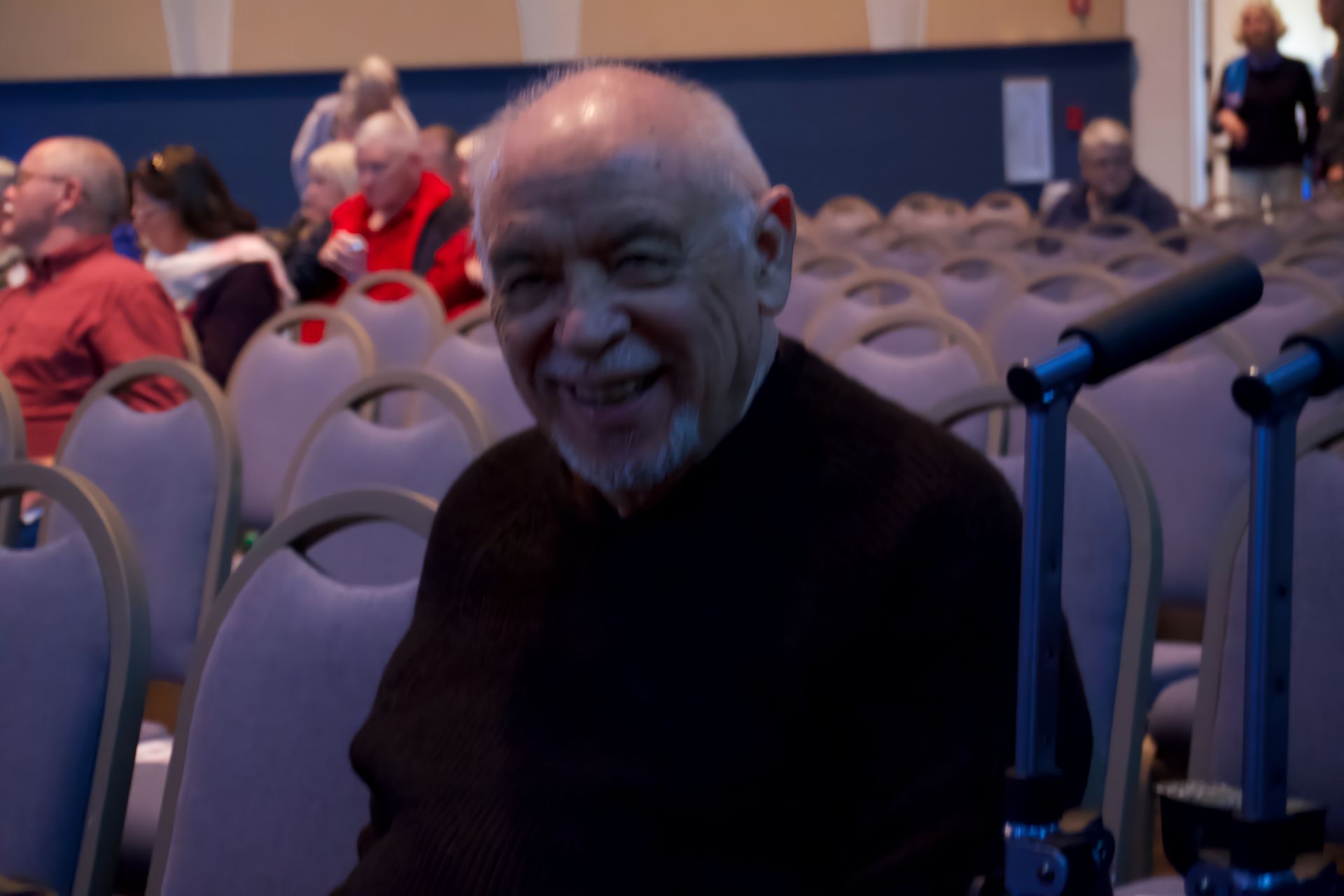A man in a wheelchair is smiling in front of a crowd of people
