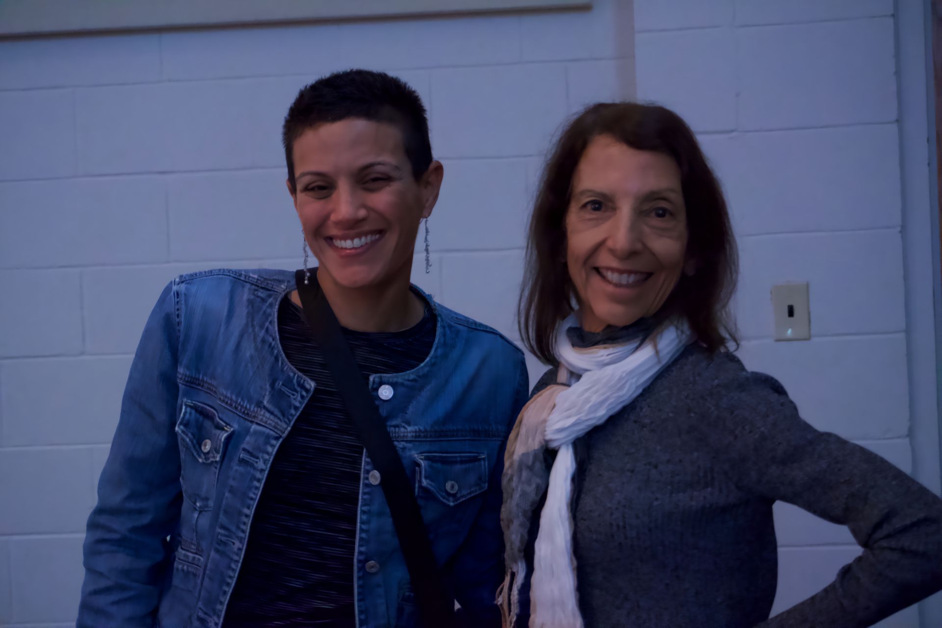 Two women are posing for a picture together in front of a white wall.