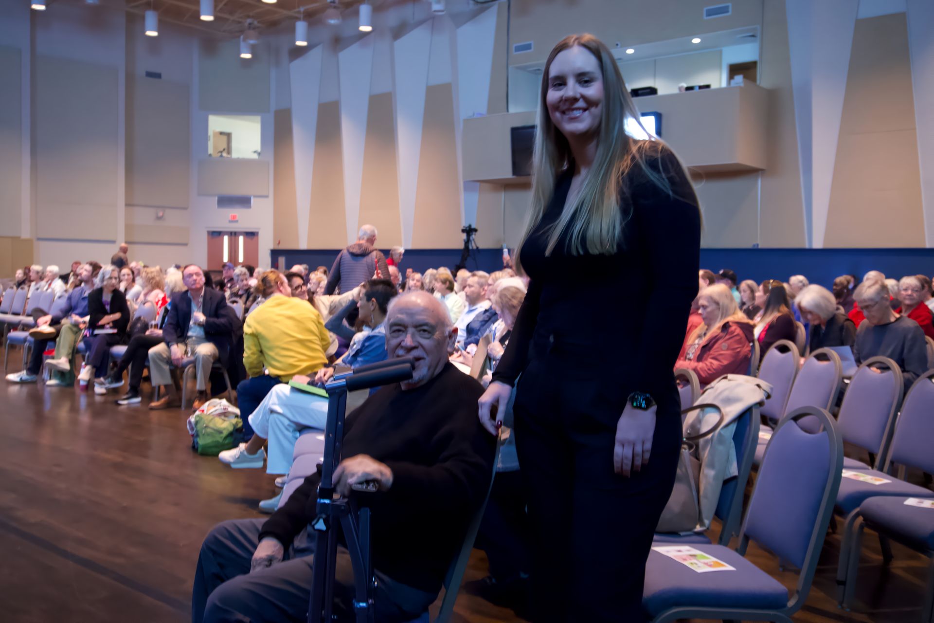 A woman is standing next to a man in a wheelchair.