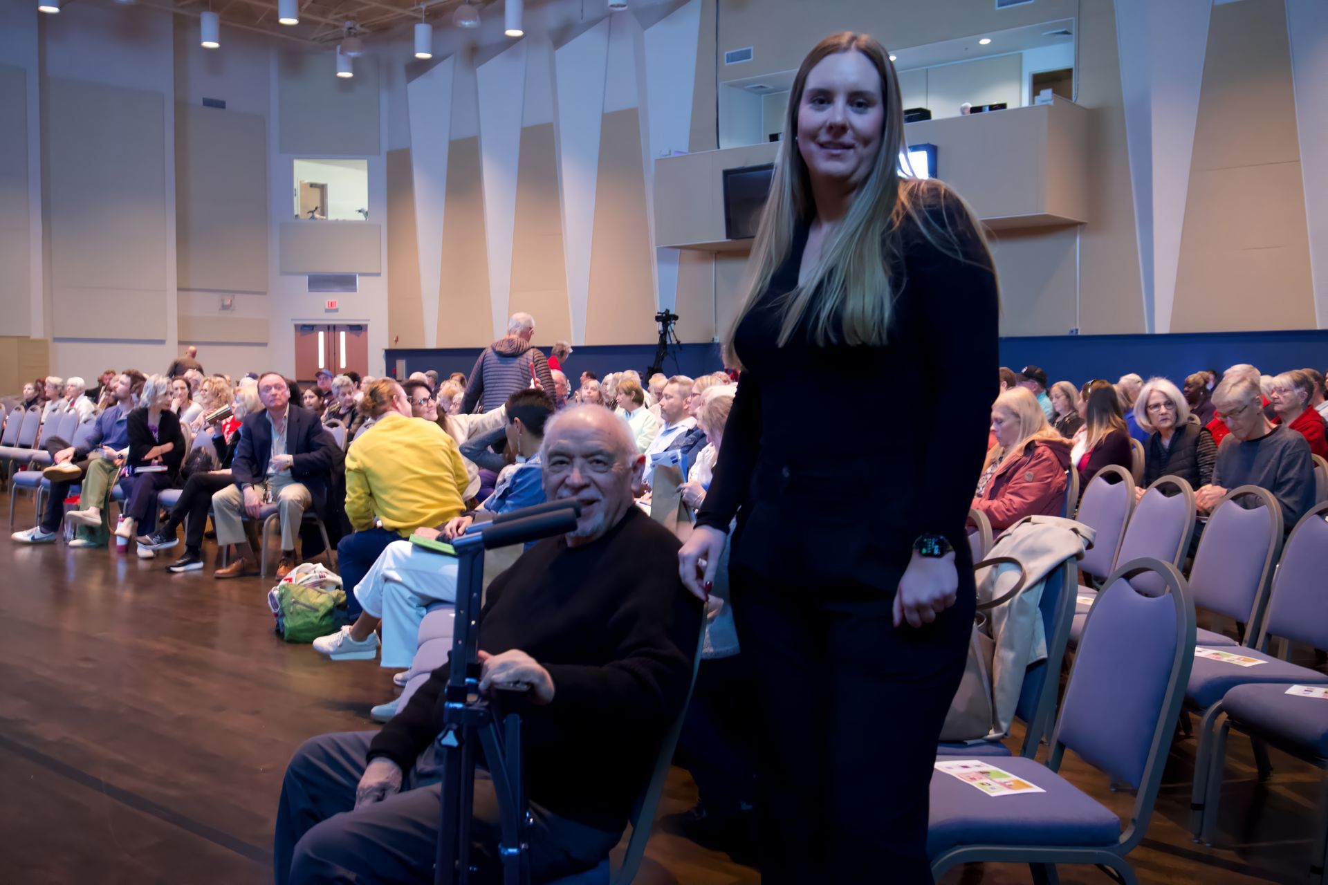 A woman is standing next to a man in a wheelchair.