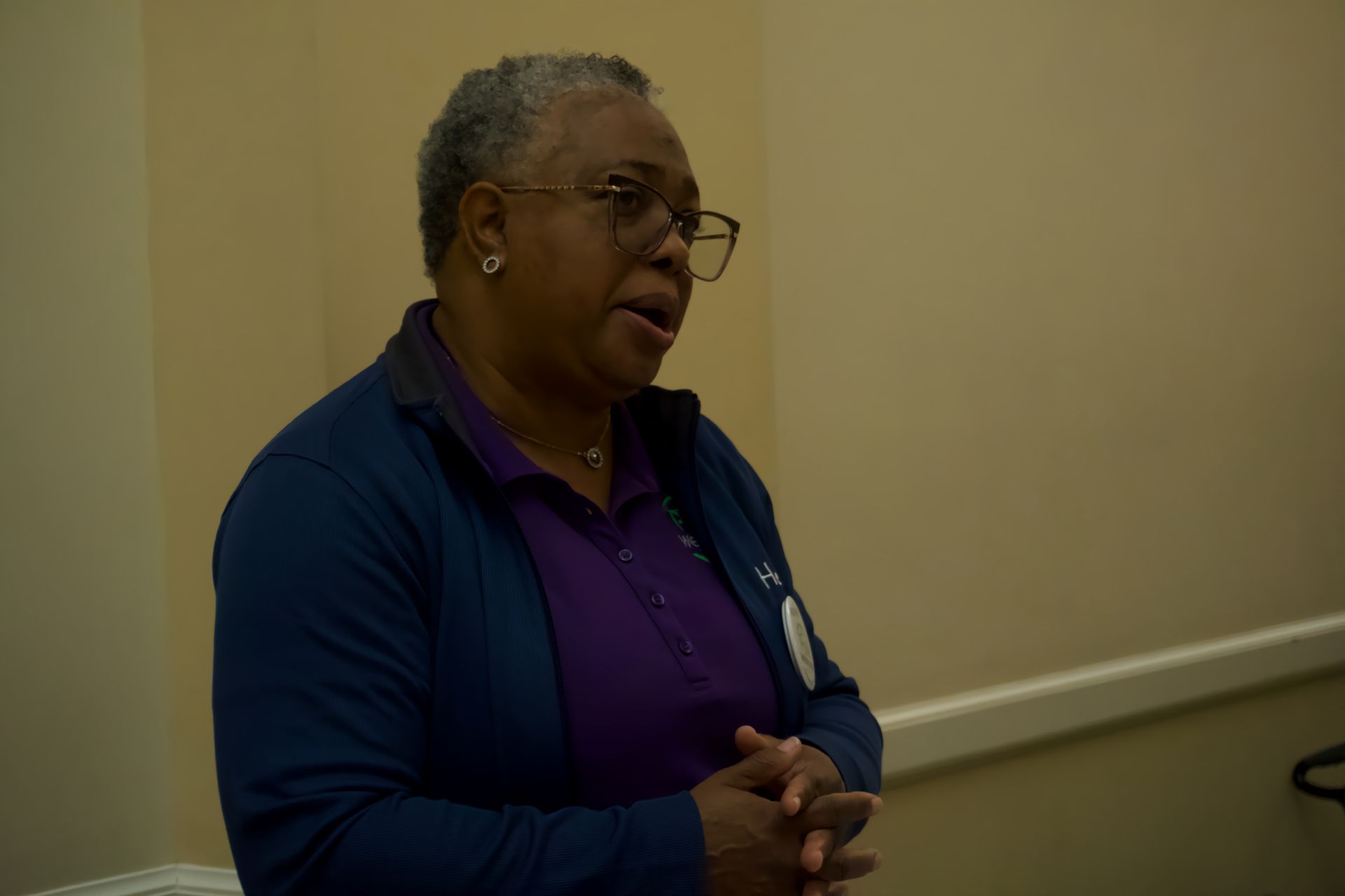 A woman wearing glasses and a blue jacket is talking to someone.