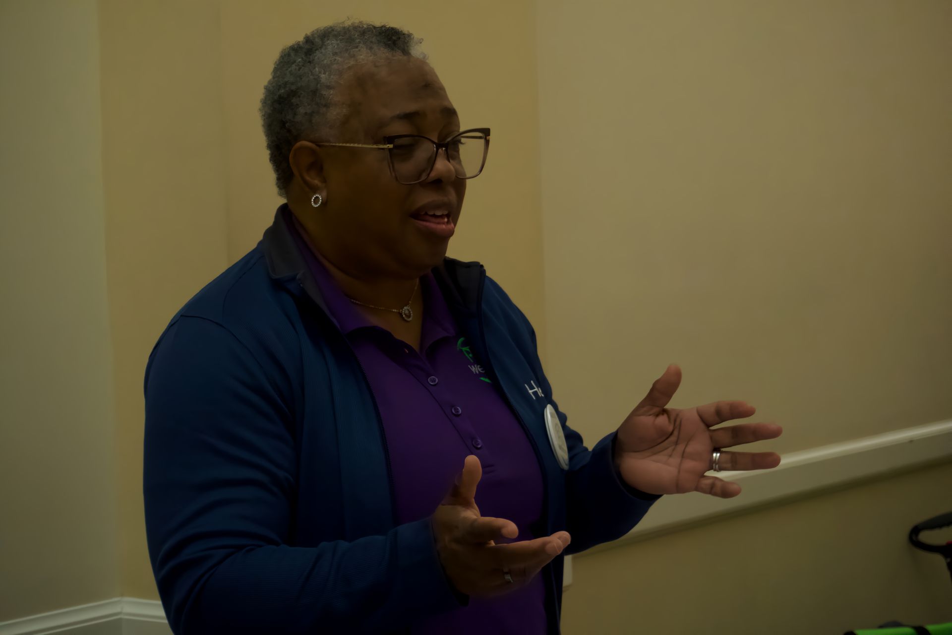 A woman in a purple shirt and blue jacket is talking to someone.