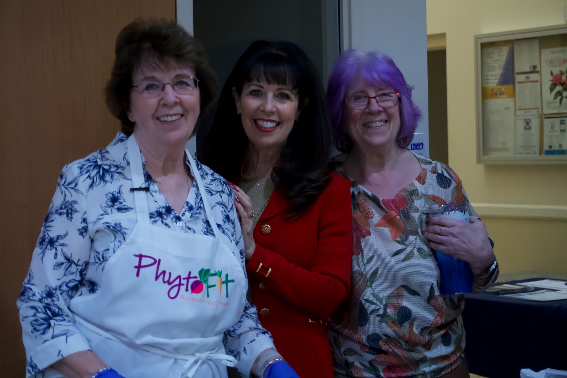 Three women are posing for a picture with one wearing an apron that says phytofit.