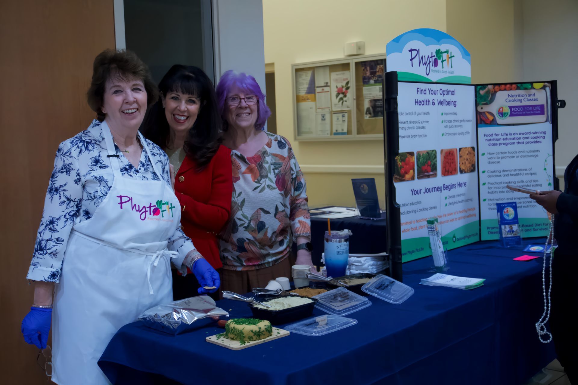 Three women are posing for a picture in front of a table with food on it.
