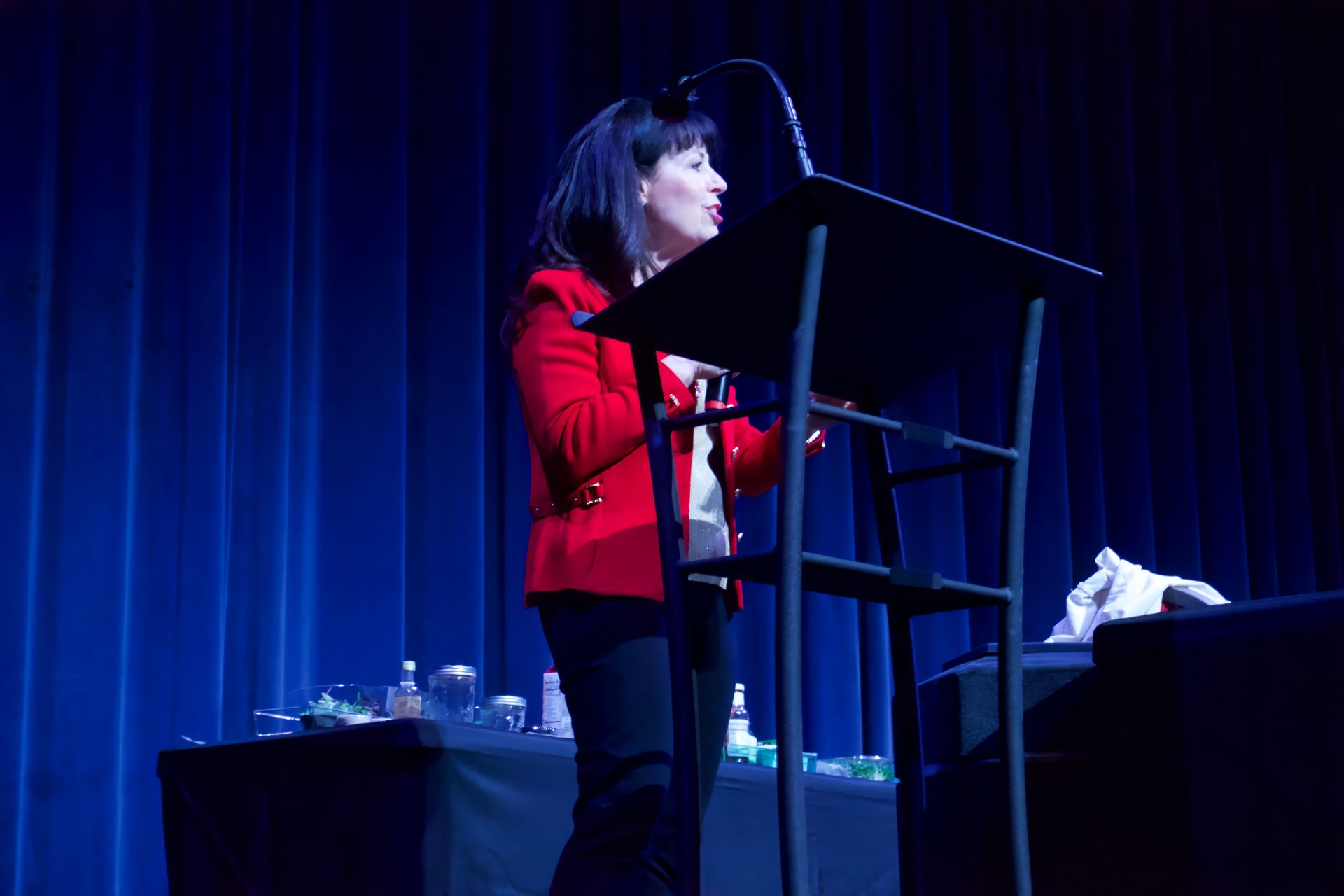 A woman in a red jacket is standing at a podium on a stage