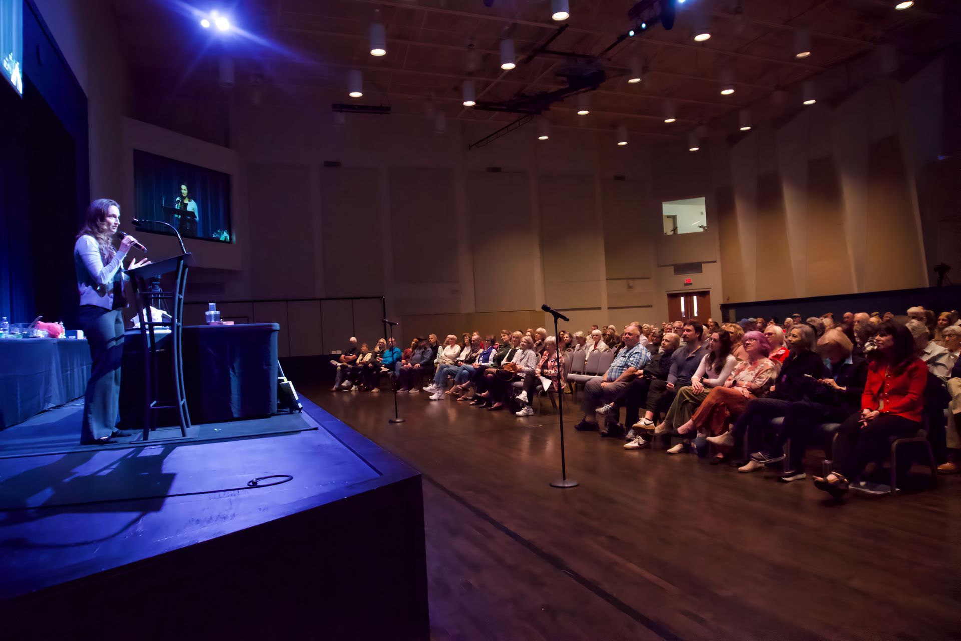 A woman is giving a presentation in front of a crowd in a large auditorium.