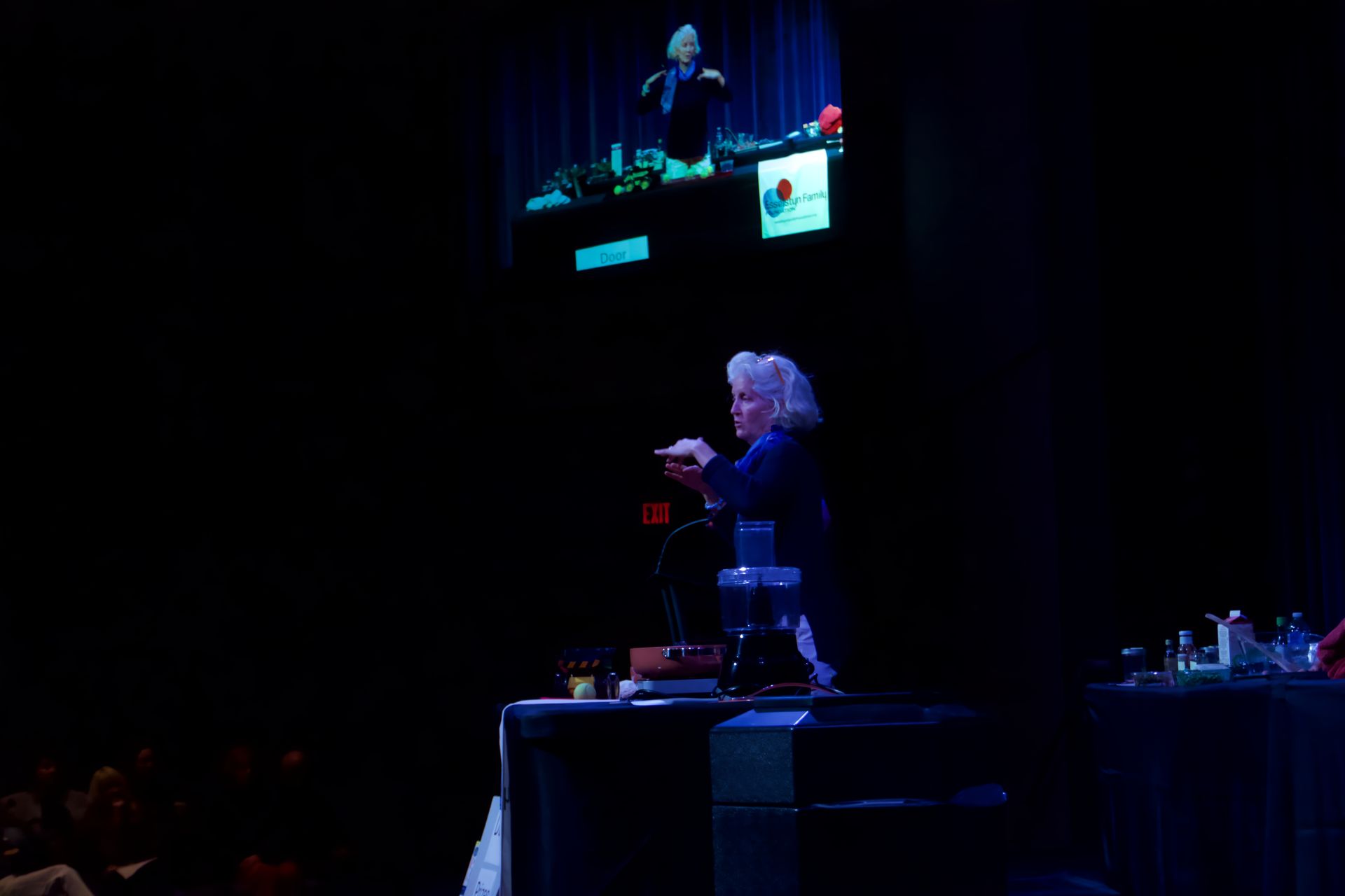 A woman is standing in front of a crowd on a stage giving a presentation.
