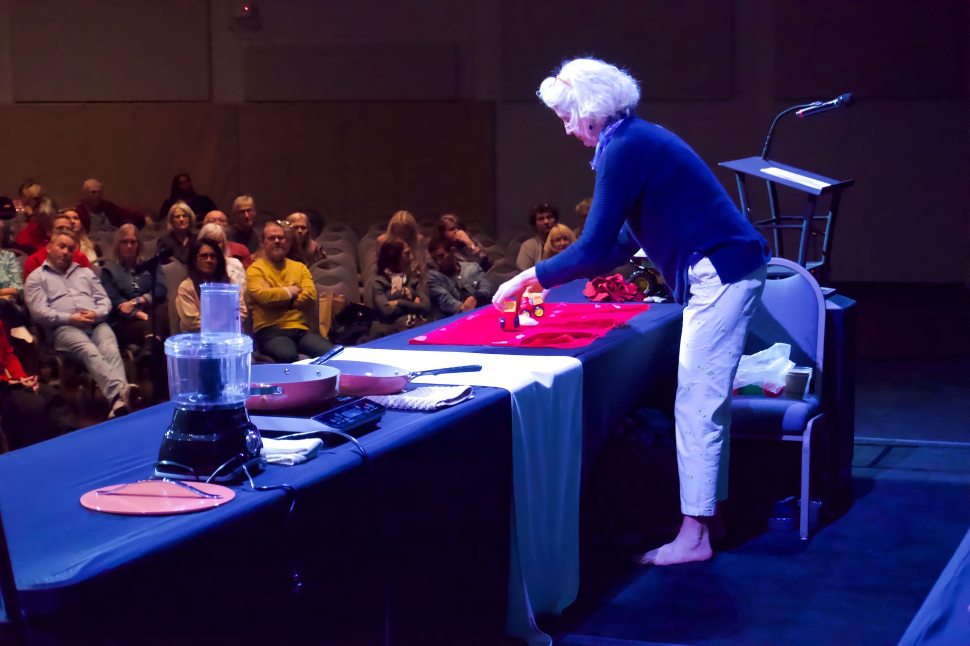 A woman is standing at a table in front of a crowd