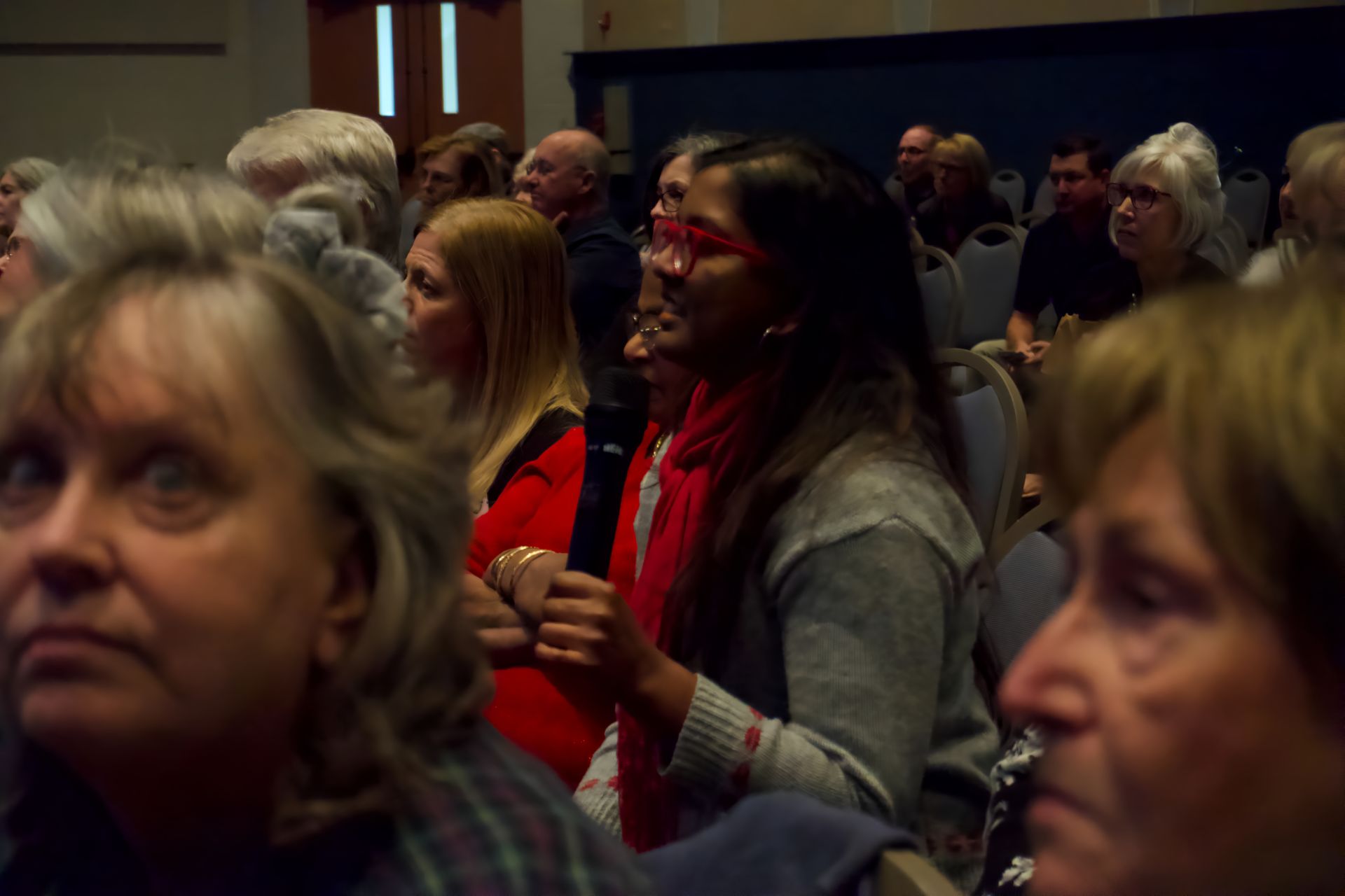 A woman in a red scarf is sitting in a crowd holding a microphone