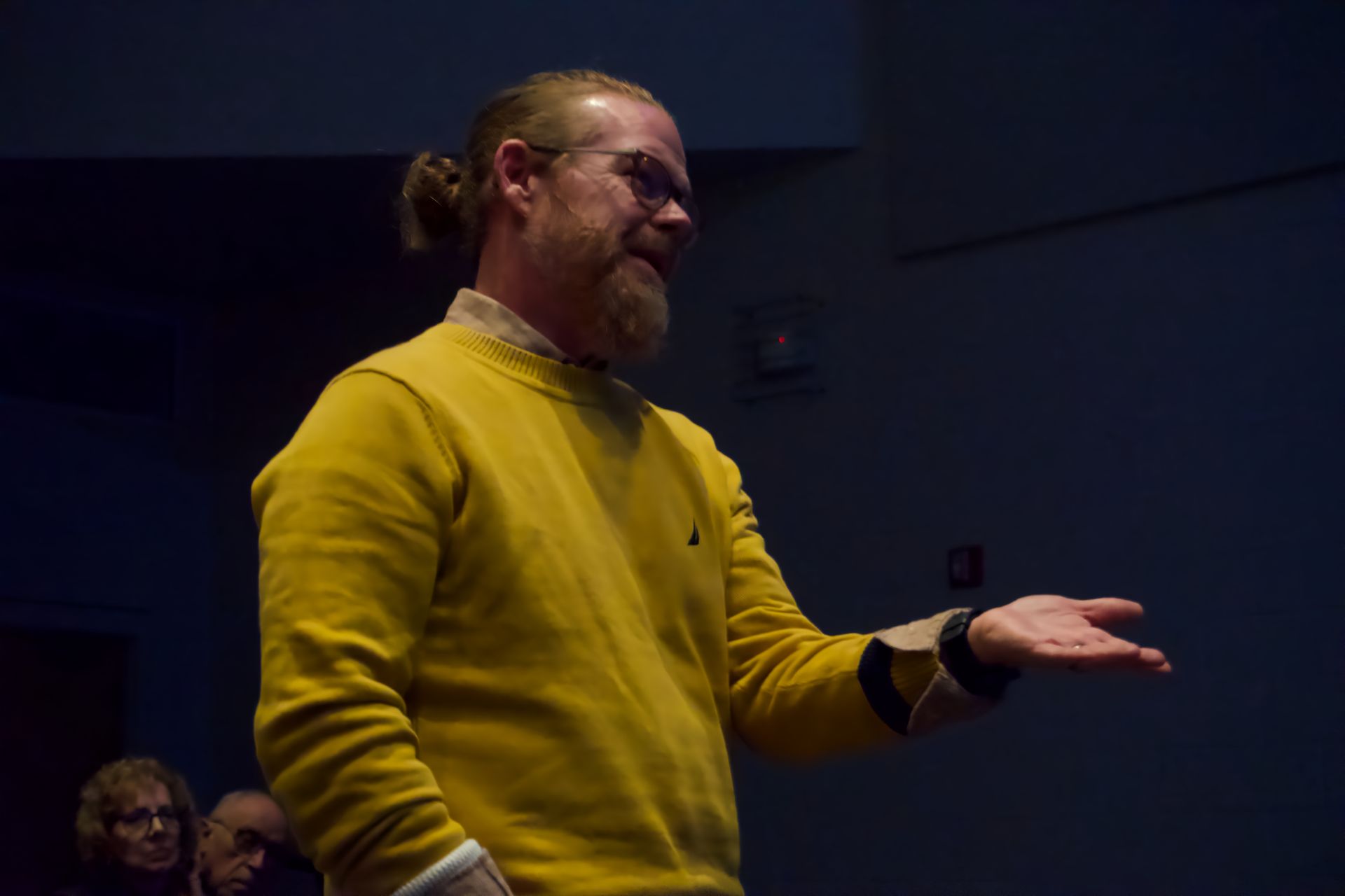 A man in a yellow sweater is standing in front of a group of people.
