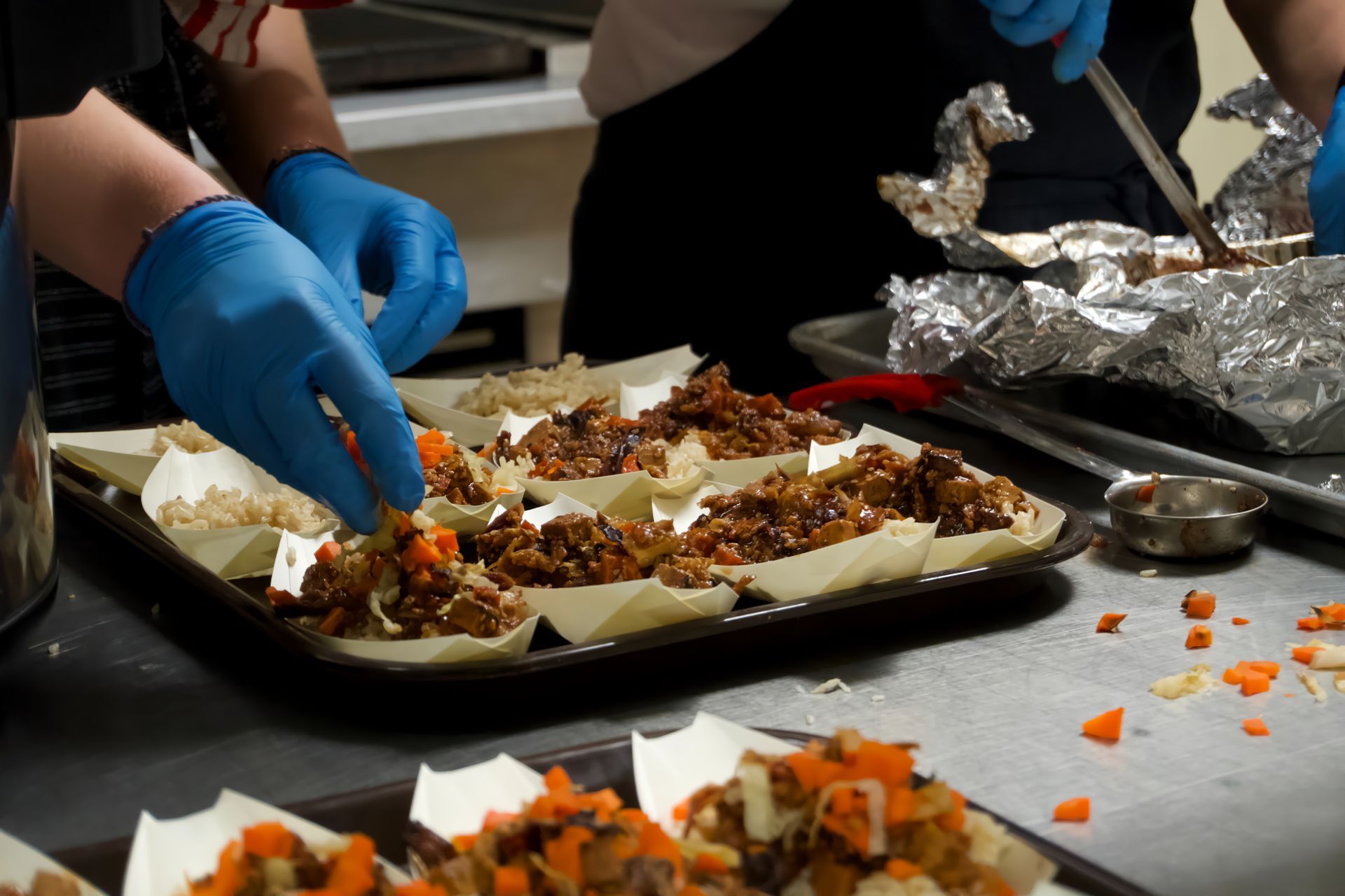 Two people wearing blue gloves are preparing food in a kitchen.